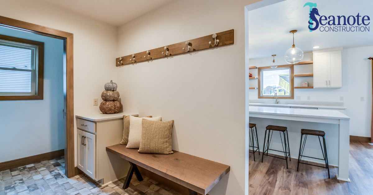 A modern home interior featuring a mudroom area with a wooden bench and hooks, leading to a bright kitchen with white cabinets and barstools.