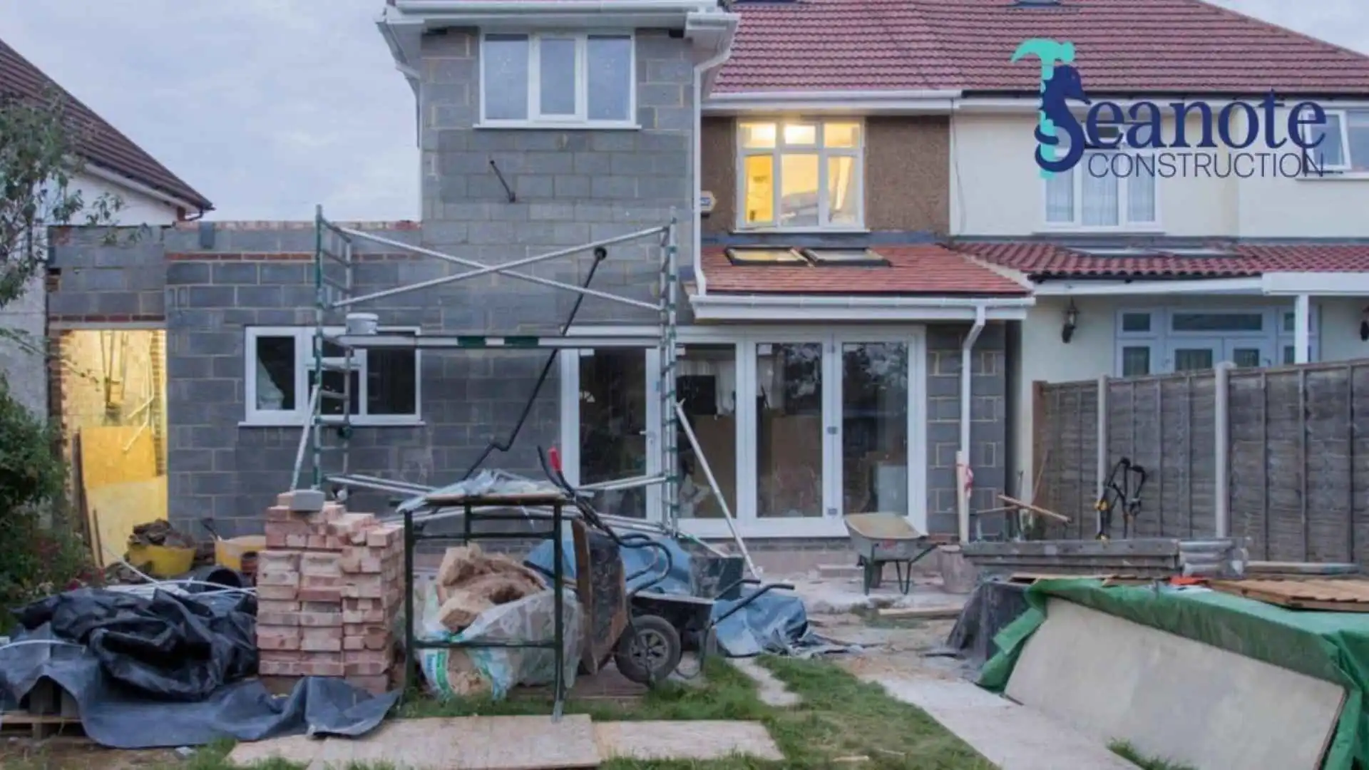 A suburban house undergoing major renovations with scaffolding and building materials, illustrating home addtions in Ponte Vedra Beach. Branded with the Seanote Construction logo.